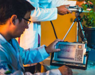 Alunos da Faculdade de Celulose e Papel em laboratório, realizando atividade prática com equipamentos de medição em plantas, focando em pesquisa.