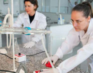 Alunas da Faculdade de Celulose e Papel em laboratório, realizando experimentos com tubos de ensaio e equipamentos de destilação, focando em pesquisa.