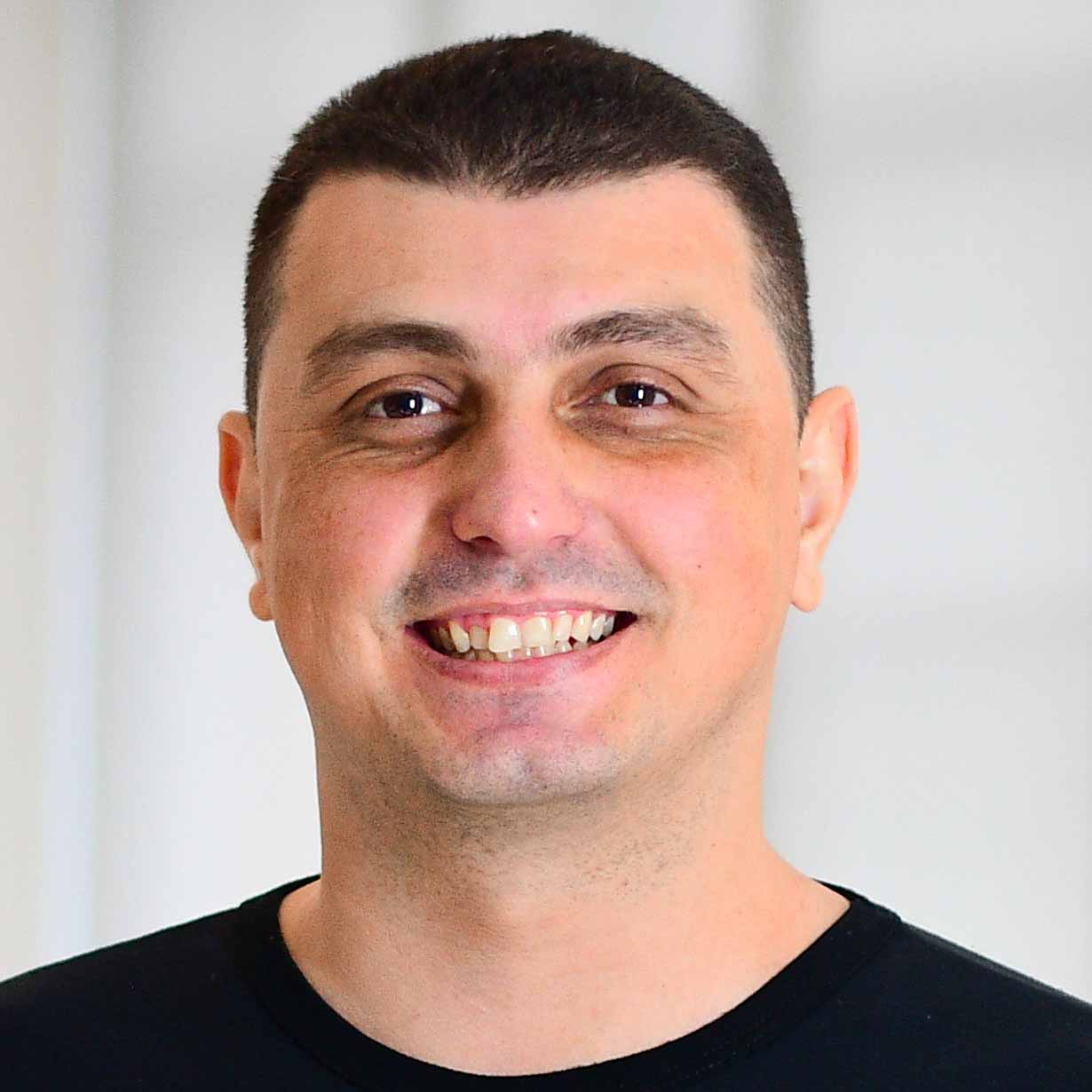 Christiano, aluno do curso de sistemas de informação, trajando uma camiseta preta. Ele está em um ambiente interno com fundo claro e minimalista, sugerindo um espaço acadêmico ou corporativo. A iluminação suave cria um contraste limpo e destaca a simplicidade e seriedade da composição.