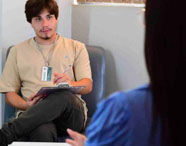 Aluno da Faculdade de Terapia Ocupacional realizando atendimento e anotações com paciente na clínica-escola, focando em avaliação e plano de tratamento.