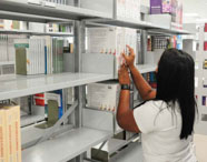 Aluna da Faculdade de Terapia Ocupacional em Guarujá selecionando um livro na prateleira da biblioteca, em busca de material para estudo e pesquisa.
