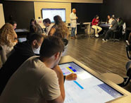 Alunas da Faculdade de Terapia Ocupacional em Guarujá em aula na Sala Betha, utilizando mesas interativas para estudos avançados em ambiente tecnológico.