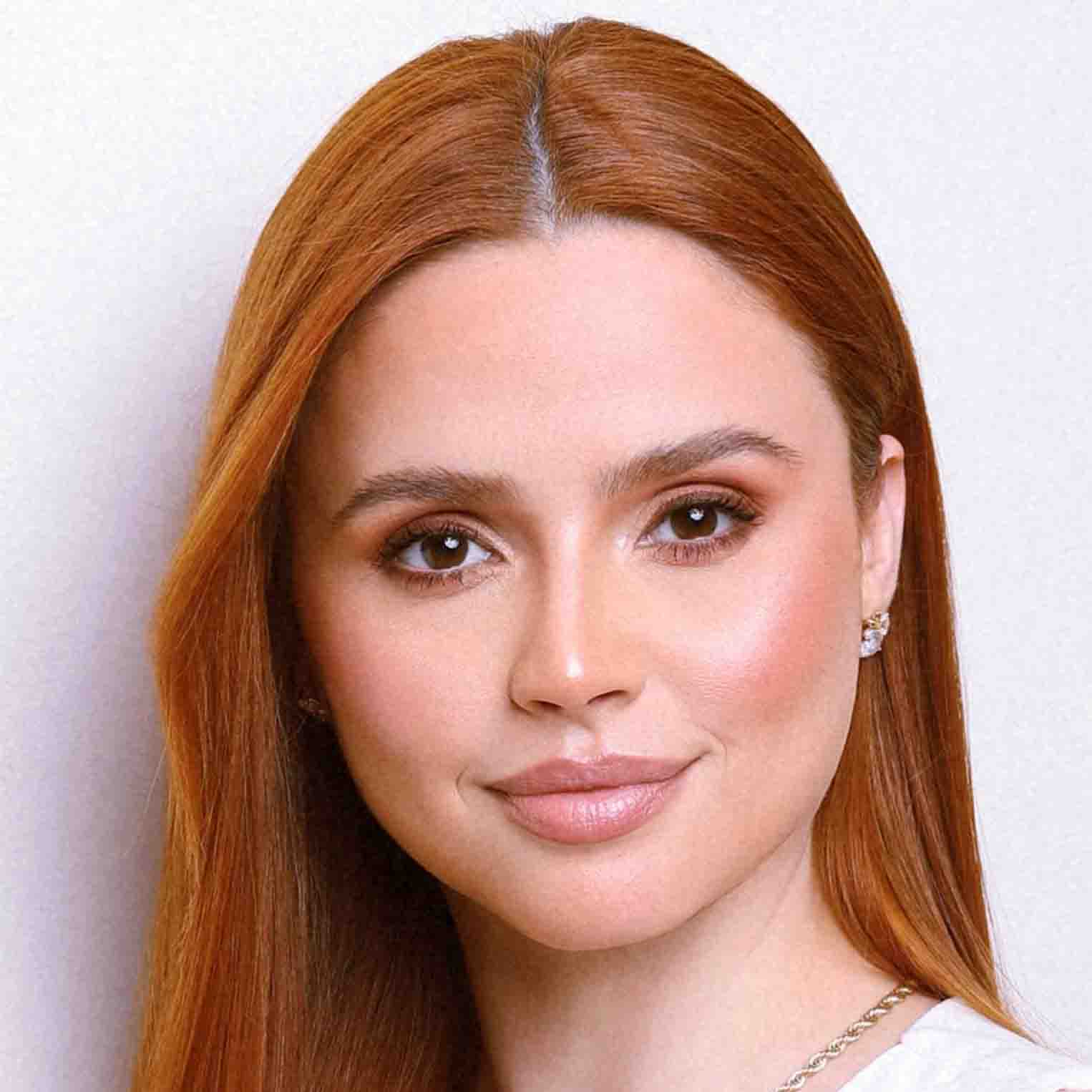 Letícia, egressa do curso de estética e cosmética, posando em um estúdio com fundo branco. Seu cabelo liso e ruivo destaca-se na composição minimalista.