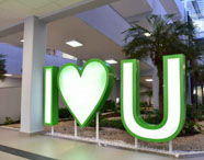 Letreiro I LOVE U em área de convivência da Faculdade de Estética e Cosmética em Guarujá, com palmeiras e arquitetura moderna.