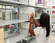 Aluna da Faculdade de Estética e Cosmética em Guarujá selecionando um livro na prateleira da biblioteca, em busca de material para estudo e pesquisa.