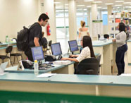 Balcão de atendimento da biblioteca da Faculdade de Estética e Cosmética em Guarujá, com alunos e funcionários, oferecendo suporte para pesquisa.