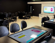 Sala Betha da Faculdade de Estética e Cosmética em Guarujá, com mesas interativas e cadeiras modernas, para aulas e projetos tecnológicos.