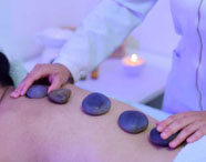 Aluna da Faculdade de Estética e Cosmética realizando massagem com pedras quentes nas costas de uma cliente, demonstrando habilidades terapêuticas.