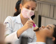 Aluna da Faculdade de Estética e Cosmética realizando atividade prática de maquiagem em modelo, demonstrando habilidades e técnicas de beleza.