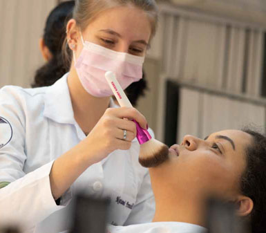 Aluna da Faculdade de Estética e Cosmética em Guarujá realizando maquiagem em modelo, demonstrando habilidades práticas e o perfil profissional do curso.