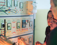 Alunos da Faculdade de Energias Renováveis em laboratório de instrumentação, operando equipamentos e painéis de controle para medições elétricas.