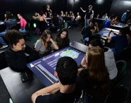Alunos da Faculdade de Energias Renováveis em aula na Sala Betha, utilizando mesas interativas para aprendizado colaborativo e tecnológico.