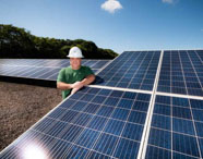 Profissional da área de Energias Renováveis em Presidente Prudente, usando capacete e camisa da Unoeste, em frente a painéis solares.