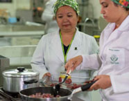 Alunas da Faculdade de Alimentos em aula prática de gastronomia, preparando alimentos em cozinha industrial, focando em técnicas culinárias e segurança alimentar.