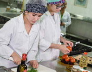 Alunas da Faculdade de Alimentos em laboratório de análise de alimentos, preparando ingredientes e realizando medições para controle de qualidade.