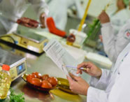 Aluna da Faculdade de Alimentos revisando anotações em laboratório de análise de alimentos, com ingredientes e equipamentos ao redor, focando em pesquisa.