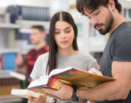 Alunos da Faculdade de Sistemas de Informação em Jaú consultando livros na biblioteca, em ambiente de estudo e pesquisa.