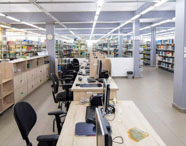 Interior da biblioteca da Faculdade de Mídias Sociais Digitais, com prateleiras de livros, mesas de estudo e computadores, ambiente ideal para pesquisa.