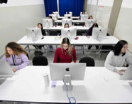 Vista geral do laboratório Mac da Faculdade de Mídias Sociais Digitais, com vários alunos utilizando computadores Apple para atividades acadêmicas.