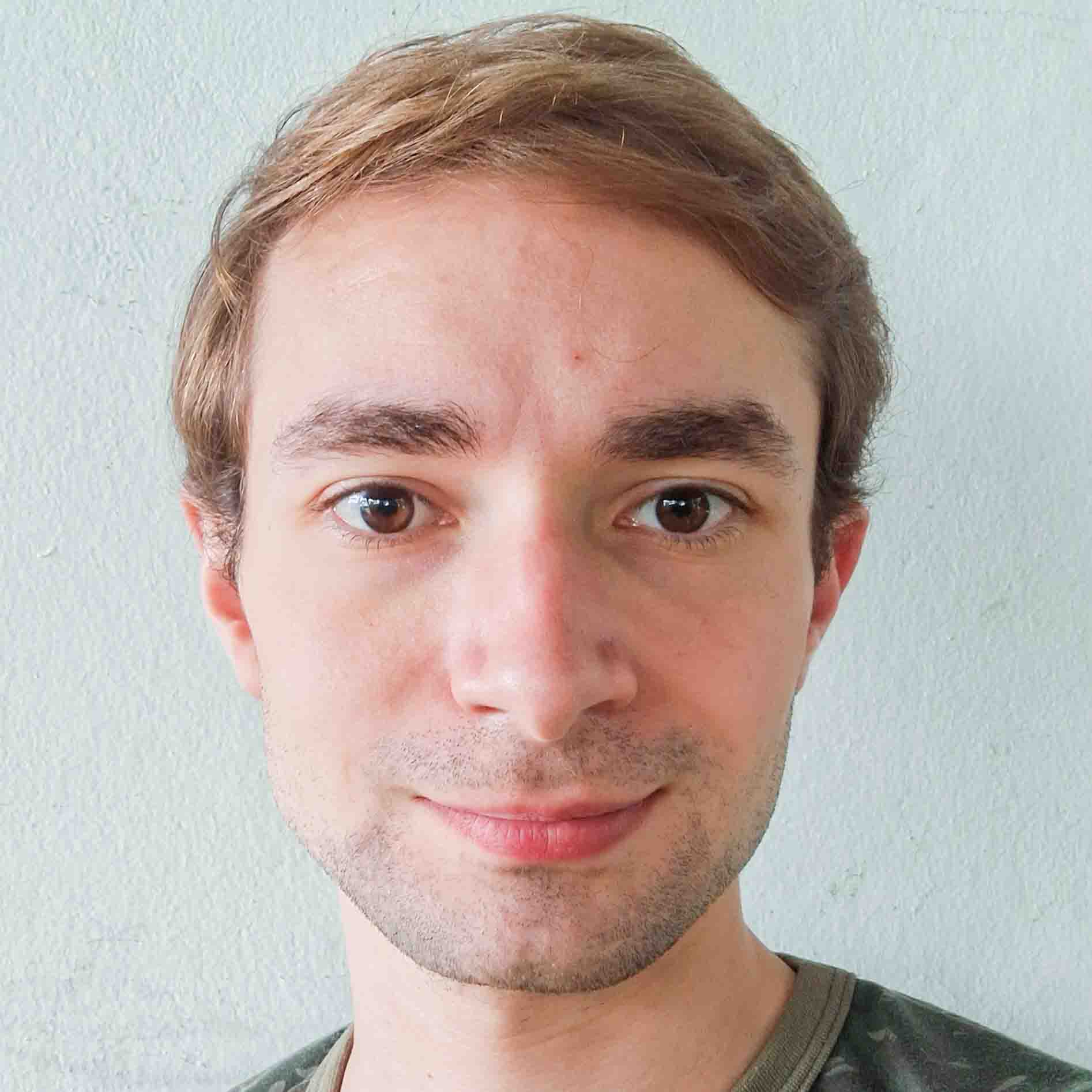 Eduardo, egresso do curso de ciências biológicas (bacharelado), posando em frente a uma parede clara que cria um contraste suave. Ele veste uma camiseta verde com estampa discreta.
