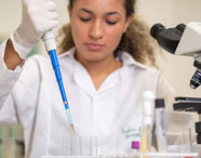 Aluna da Faculdade de Ciências Biológicas em laboratório, manuseando pipeta e tubos de ensaio, realizando experimentos e análises científicas.