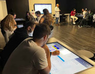 Alunos da Faculdade de Ciências Biológicas em Guarujá em aula na Sala Betha, utilizando mesas interativas para aprendizado colaborativo e tecnológico.