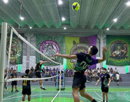 Jogo de vôlei no ginásio de esportes da Faculdade de Ciências Biológicas em Guarujá, com atletas em ação e torcida nas arquibancadas.