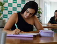 Aluna da Faculdade de Agronomia em Jaú concentrada em seus estudos em sala de aula, escrevendo em caderno.