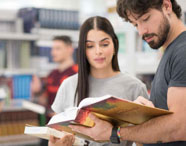Dois alunos da Faculdade de Agronomia em Jaú consultando livros na biblioteca, em ambiente de estudo e pesquisa.