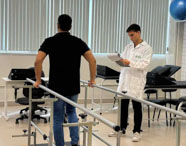 Atendimento de paciente em clínica de fisioterapia da Faculdade de Terapia Ocupacional em Jaú, com aluno auxiliando na reabilitação em barras paralelas.