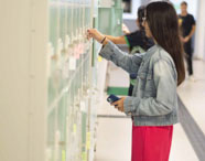 Aluna da Faculdade de Estética e Cosmética em Jaú utilizando armário no corredor do campus, com outros estudantes ao fundo.