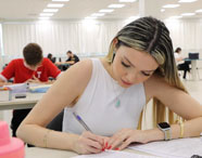 Estudante da Faculdade de Estética e Cosmética em Jaú concentrada em seus estudos, escrevendo em caderno em ambiente de sala de aula.