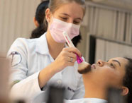 Aluna da Faculdade de Estética e Cosmética realizando atividade prática de maquiagem em modelo, demonstrando habilidades e técnicas de beleza.