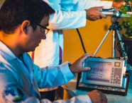Alunos da Faculdade de Biotecnologia em laboratório, realizando atividade prática com equipamentos de medição em plantas, focando em pesquisa.