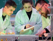 Professor da Faculdade de Biotecnologia orientando alunos em laboratório, com equipamentos de pesquisa e experimentos científicos.