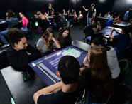 Alunos da Faculdade de Biotecnologia em aula na Sala Betha, utilizando mesas interativas para aprendizado tecnológico e colaborativo.