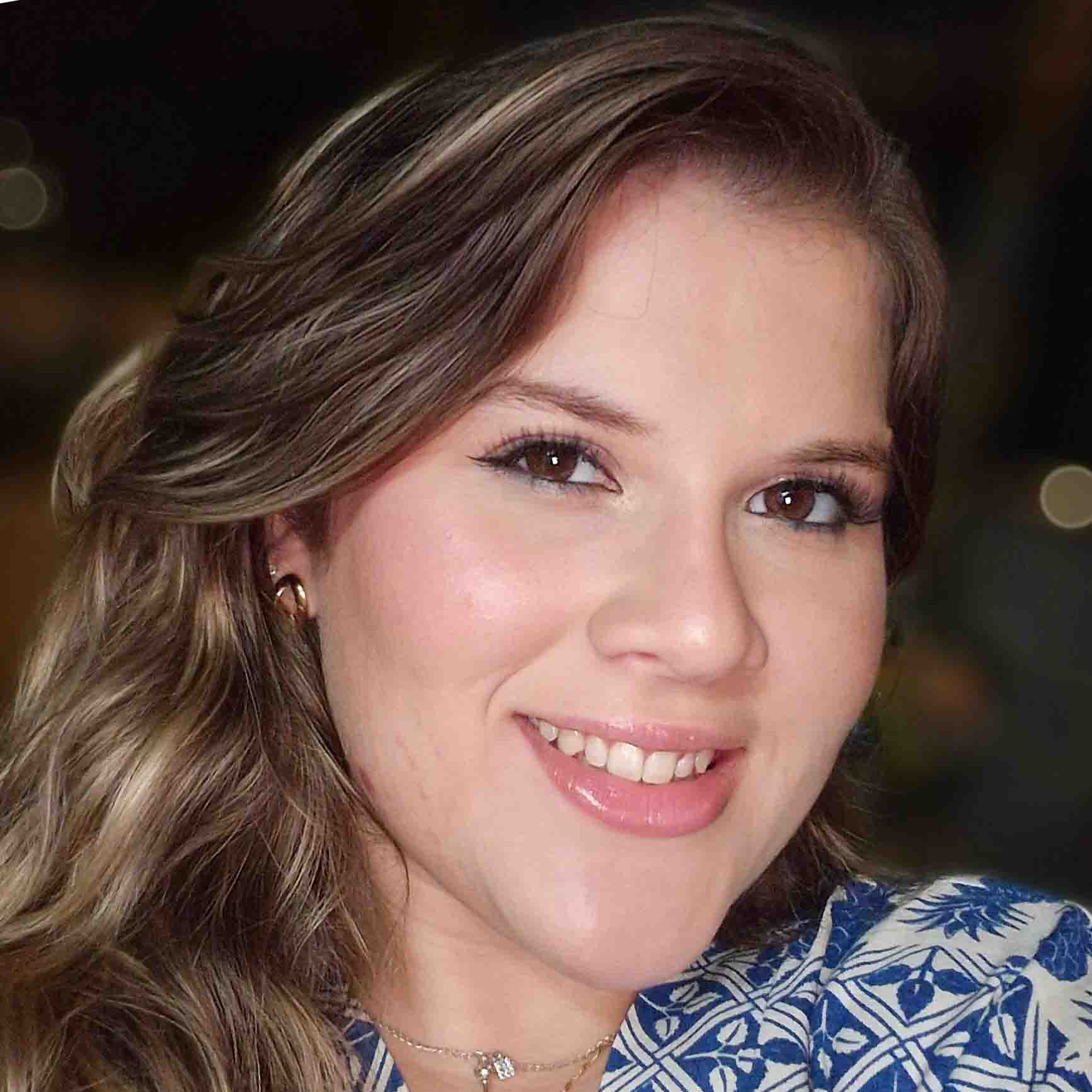 Luara, aluna do curso de ciências contábeis, em um ambiente noturno com iluminação suave e detalhes desfocados ao fundo. Ela veste uma blusa azul com estampas brancas, criando um visual elegante.
