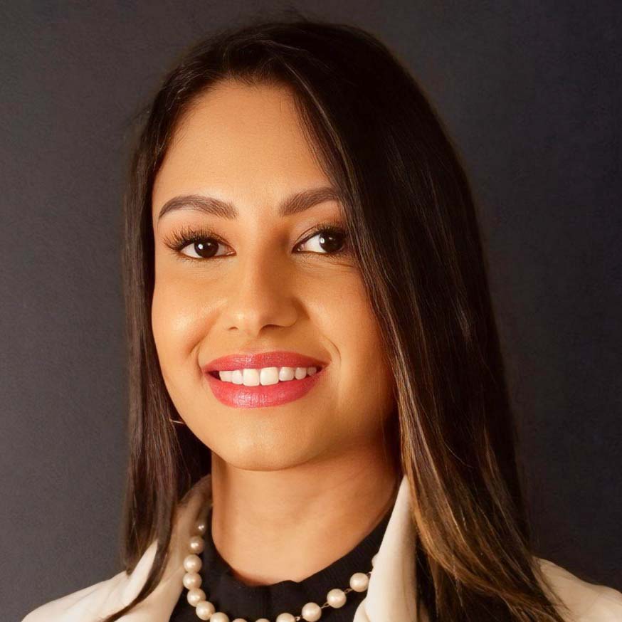 Thais, egressa do curso de ciências contábeis, usando um colar de pérolas e blazer claro sobre uma blusa preta. O fundo escuro destaca sua postura profissional e sofisticada.