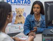 Duas estudantes do curso de Ciências Contábeis da Unoeste participam de atendimento na empresa júnior. Uma delas veste jaqueta jeans e gesticula, enquanto a outra, de óculos, observa. Ao fundo, banner com leão e palavras relacionadas à área contábil, além de computador sobre a mesa.