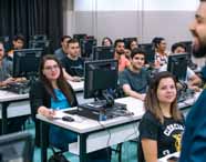 Sala de laboratório de informática com diversos alunos do curso de Ciências Contábeis da Unoeste em Presidente Prudente. Estudantes estão sentados diante de computadores, atentos ao professor que aparece parcialmente à direita, em ambiente iluminado e organizado.