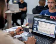 Aluno do curso de Ciências Contábeis da Unoeste em Presidente Prudente realiza atividade prática. Ele segura uma calculadora científica enquanto digita no notebook, acompanhado de colegas ao fundo. A tela exibe conteúdo sobre reservas de capital, destacando o aprendizado aplicado.