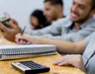 Em sala de aula da Unoeste, alunos do curso de Ciências Contábeis realizam atividades práticas. Calculadora científica e caderno espiral aparecem em destaque sobre bancada de madeira clara, enquanto estudantes escrevem e resolvem exercícios, focados no aprendizado contábil.