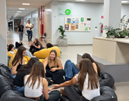 Alunas sentadas em pufes, conversando e interagindo em uma área de convivência interna do campus de Jaú, com corredores, murais e outros estudantes ao fundo.