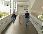 Três estudantes universitários sorridentes caminhando lado a lado em uma rampa interna acessível e bem iluminada na Unoeste Jaú.