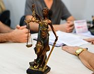 Estátua de bronze da Deusa da Justiça (Têmis) segurando a balança e a espada em destaque sobre uma mesa de escritório.