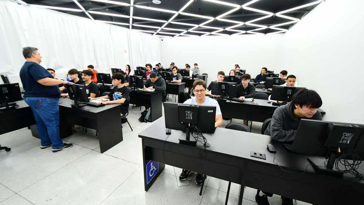 Professor orienta alunos de Sistemas de Informação em aula prática no laboratório de informática, focando em desenvolvimento e aplicação de conceitos de programação e TI.