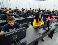 Estudantes da Faculdade de Sistemas de Informação em atividade prática no laboratório de informática, utilizando computadores individuais em sala moderna.