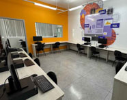 Laboratório de informática da Faculdade de Sistemas de Informação com computadores dispostos em bancada única e parede com arte digital.