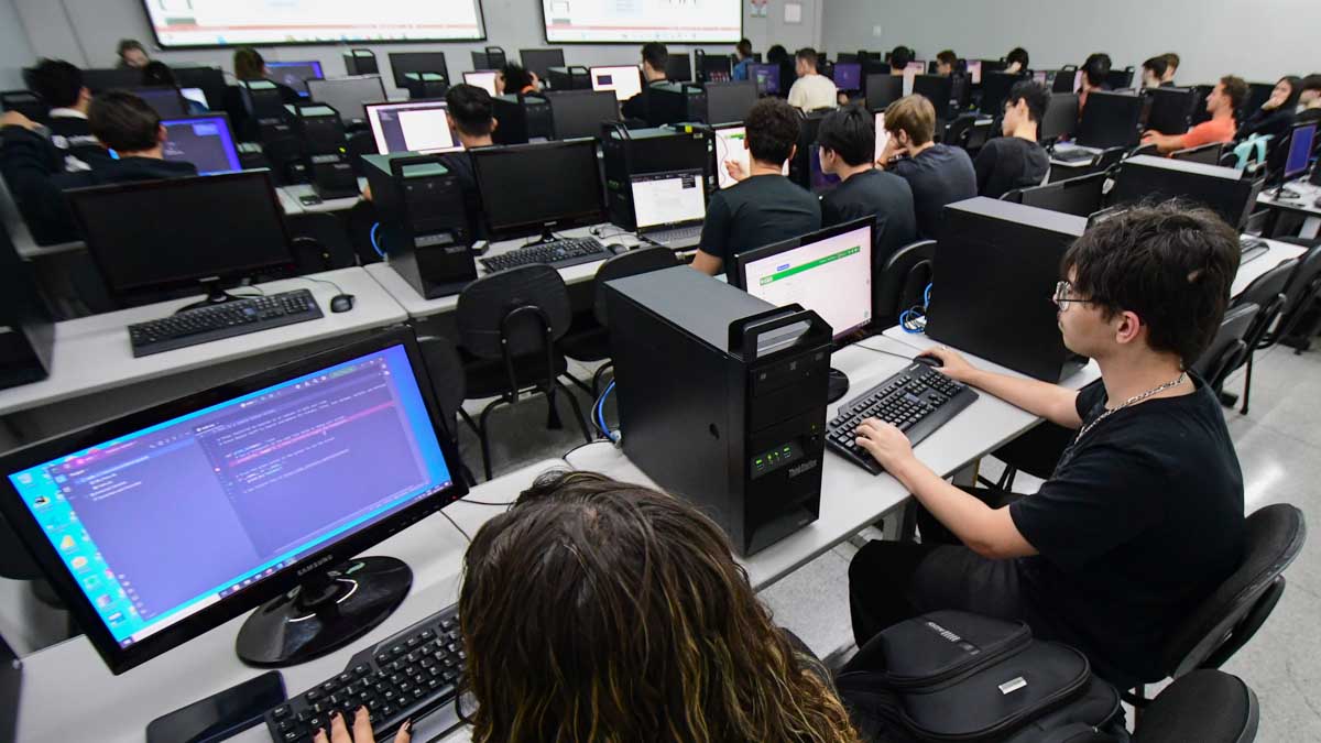 Alunos da faculdade de Sistemas de Informação em aula prática de programação (Python) no laboratório, desenvolvendo códigos e soluções tecnológicas.
