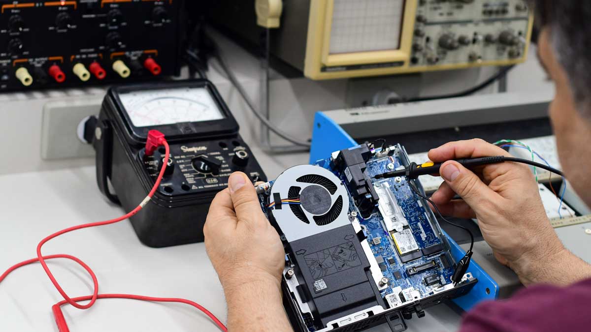 Técnico de Sistemas de Informação realizando manutenção e teste de hardware em um microcomputador, utilizando equipamentos de medição em laboratório de arquitetura de computadores.